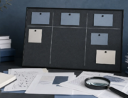 Incomplete unmarked planning board with research papers and a magnifying glass on a blue-gray desk.
